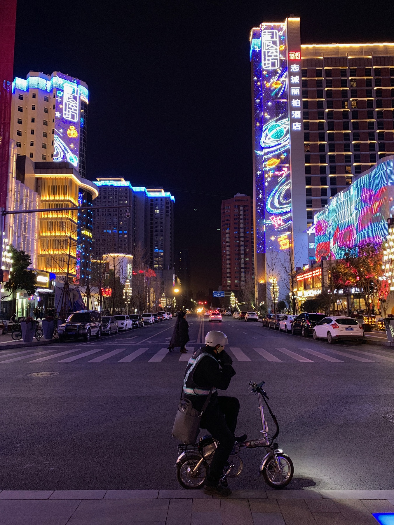 A cyclist crossing a neon-lit city street at night