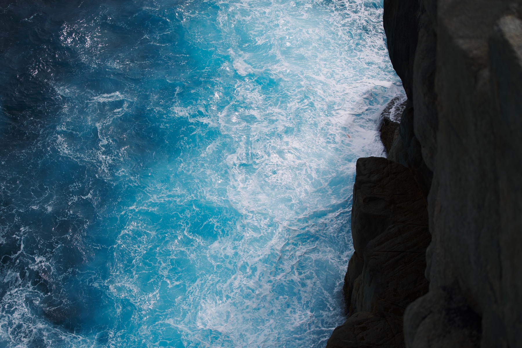 Waves crashing below a dark cliff